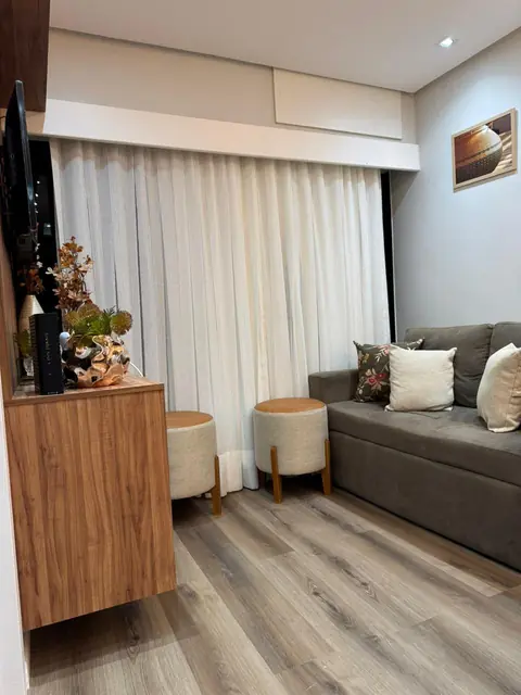Sala com sofá cinza, banquetas e rack de madeira, com cortina até o chão