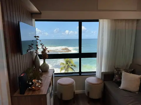 Sala com rack de madeira, banquetas e janela com vista para o mar
